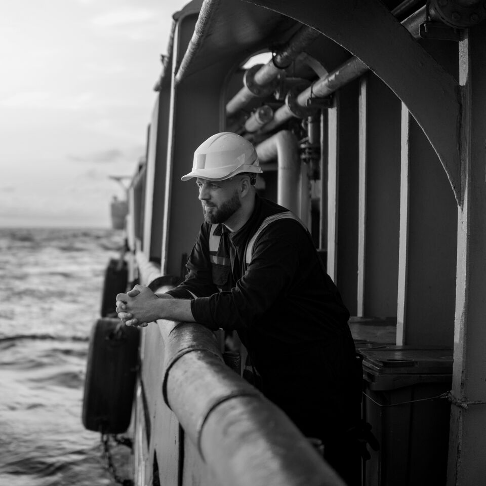 SINGLE-IMAGE_male-worker-clasped-hands-on-boat-looking-to-sea-black-and-white_jul24